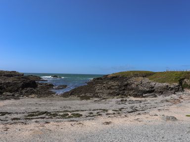 A rocky beach with seaweed patches and grassy hills under a clear blue sky at Seaside Sanctuary in Trearddur Bay