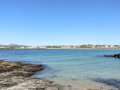A rocky shoreline with clear water and distant buildings under a clear sky at Seaside Sanctuary in Trearddur Bay