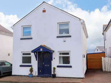 A white two-story house with blue door and window frames and two potted plants at Seaside Sanctuary in Trearddur Bay