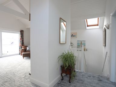 A hallway with a plant on a wooden stand and stairway with skylight and paintings at Seaside Sanctuary in Trearddur Bay
