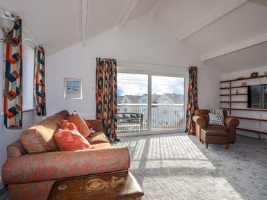 A living room with a sofa and armchair near sliding glass doors with patterned curtains at Seaside Sanctuary in Trearddur Bay