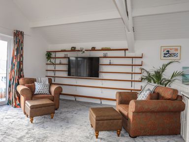 A living room with two armchairs a television on wall shelves and a potted plant at Seaside Sanctuary in Trearddur Bay