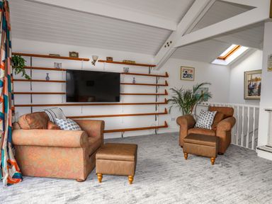 A sitting area with two armchairs a television on shelves and a skylight at Seaside Sanctuary in Trearddur Bay