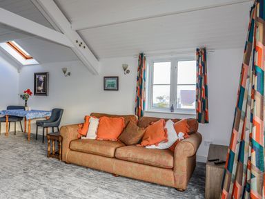 A sitting room with a patterned sofa and orange cushions near a window with patterned curtains and a small dining table with chairs at Seaside Sanctuary in Trearddur Bay