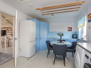 A kitchen with blue cabinets a white refrigerator a glass table with four chairs and two washing machines at Seaside Sanctuary in Trearddur Bay