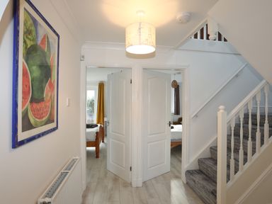 A hallway with two open doors leading to bedrooms and a staircase with carpeted steps at Seaside Sanctuary in Trearddur Bay