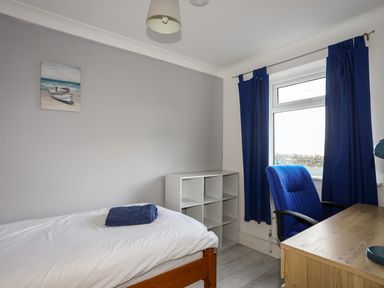 A bedroom with a single bed a desk chair and blue curtains at Seaside Sanctuary in Trearddur Bay
