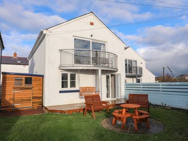 A backyard with wooden chairs a sandbox and a swing attached to a balcony at Seaside Sanctuary in Trearddur Bay