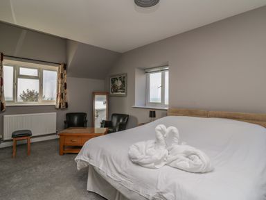 A bedroom with a bed with towel swans a wooden table two black chairs a window and a standing mirror at Mynydd ar Mor in Barmouth