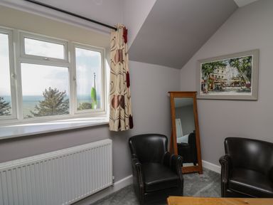 A room with two black armchairs a wooden framed mirror a window with curtains and a painting on the wall at Mynydd ar Mor in Barmouth