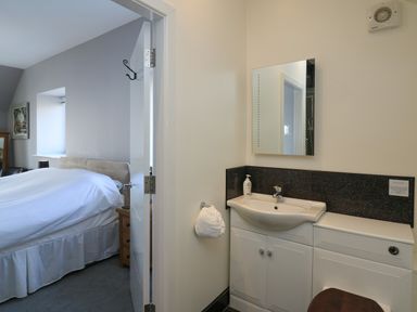 A bedroom with a bed visible through an open door next to a bathroom sink and mirror at Mynydd ar Mor in Barmouth