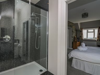 A shower area with a glass door next to a bedroom with a bed a dresser and a window at Mynydd ar Mor in Barmouth