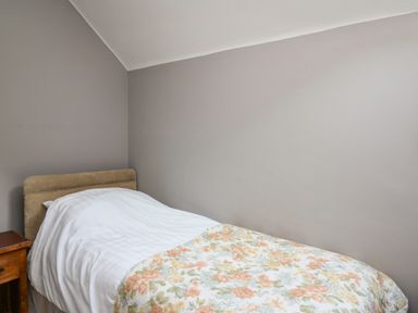 A single bed with a floral bedspread and white sheets next to a wooden nightstand in a bedroom at Mynydd ar Mor in Barmouth