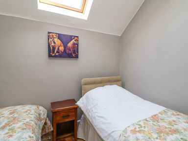 A small bedroom with two beds a wooden nightstand and a skylight window at Mynydd ar Mor in Barmouth