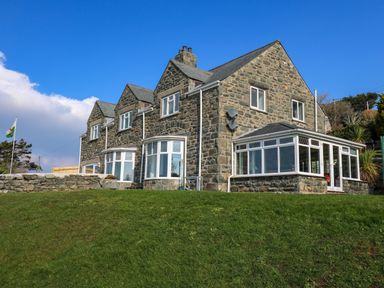 A stone house with white framed windows and a conservatory on a grassy hill at Mynydd ar Mor in Barmouth
