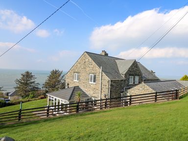 A stone house with a sloped roof and a fenced grassy yard near the sea at Mynydd ar Mor in Barmouth