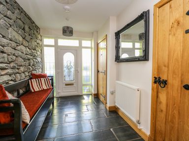 An entrance hallway with a stone wall bench with red cushions a wooden door a radiator and a wall mirror at Mynydd ar Mor in Barmouth