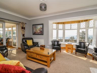 A living room with leather chairs and a wooden coffee table near a bay window with a sea view at Mynydd ar Mor in Barmouth