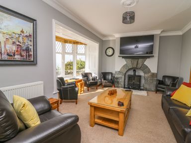 A living room with leather sofas chairs a wooden coffee table a fireplace and a wall-mounted TV at Mynydd ar Mor in Barmouth