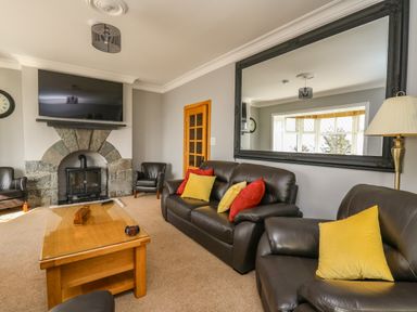 A living room with leather sofas yellow and red cushions a wooden coffee table stone fireplace and a large mirror at Mynydd ar Mor in Barmouth