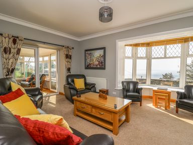 A living room with leather armchairs and a wooden coffee table near a large window with a sea view at Mynydd ar Mor in Barmouth