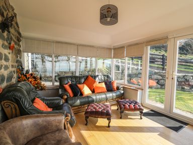 A sitting area with leather sofas orange pillows footstools and large windows at Mynydd ar Mor in Barmouth