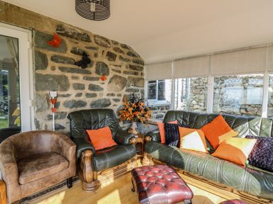 A seating area with leather armchairs a sofa and a footstool by a stone wall and windows at Mynydd ar Mor in Barmouth