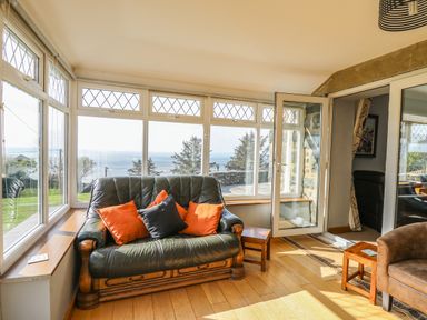 A seating area with a leather sofa and cushions next to large windows overlooking the sea at Mynydd ar Mor in Barmouth
