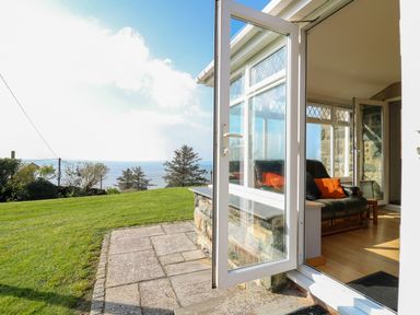 A view from an open door showing a grassy yard and trees with a view of the sea at Mynydd ar Mor in Barmouth