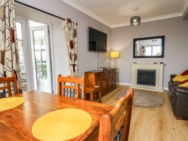 A living room with wooden dining table yellow placemats a fireplace a wall mounted tv and a brown leather sofa at Mynydd ar Mor in Barmouth
