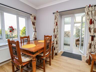A dining room with a wooden table and four chairs near windows and glass doors at Mynydd ar Mor in Barmouth