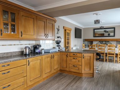 A kitchen with wooden cabinets a coffee maker kettle and a dining table with chairs at Mynydd ar Mor in Barmouth