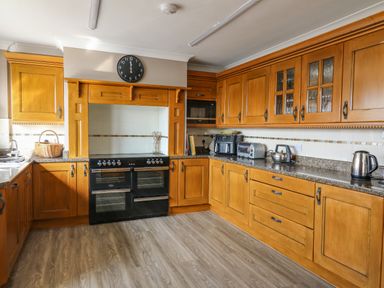 A kitchen with wooden cabinets a black double oven a black clock on the wall and various kitchen appliances on the counter at Mynydd ar Mor in Barmouth