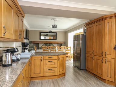 A kitchen with wooden cabinets and an island with dining table and chairs in the background at Mynydd ar Mor in Barmouth