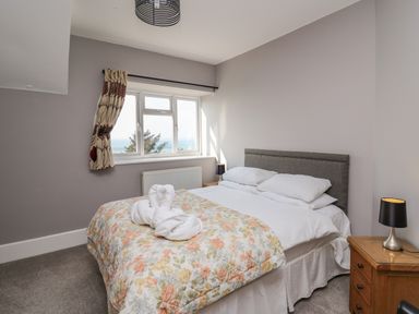 A bedroom with a double bed with floral bedding a bedside table with a lamp and a window with patterned curtains at Mynydd ar Mor in Barmouth