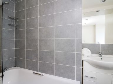 A bathroom with a bathtub and grey tiled walls at Mynydd ar Mor in Barmouth