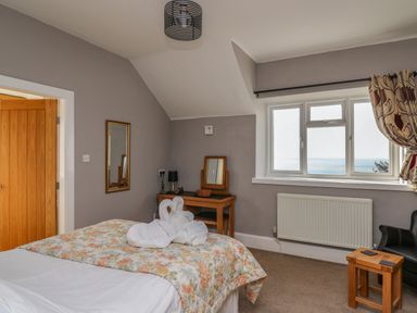 A bedroom with a bed and folded towel swans a wooden vanity table a window with curtains and a radiator at Mynydd ar Mor in Barmouth