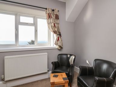 A seating area with two black armchairs and a wooden table under a window with patterned curtains at Mynydd ar Mor in Barmouth