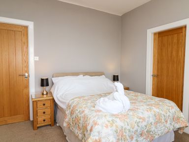 A bedroom with a floral bedspread and towel sculpture on the bed at Mynydd ar Mor in Barmouth