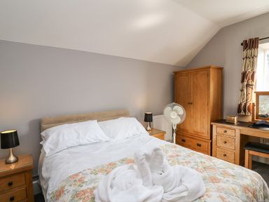 A bedroom with a bed a wooden wardrobe a desk a chair and a towel folded like swans on the bed at Mynydd ar Mor in Barmouth