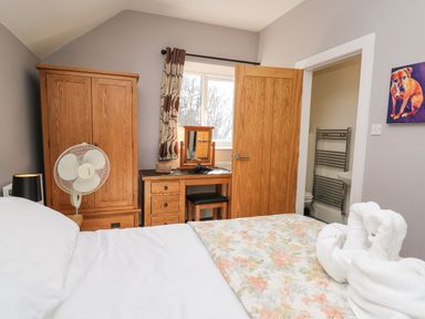 A bedroom with a wooden wardrobe dressing table and fan and an open door leading to a bathroom at Mynydd ar Mor in Barmouth