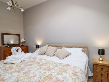 A bedroom with a bed covered in white and floral bedding two bedside tables with lamps and a wooden dresser with a mirror at Mynydd ar Mor in Barmouth