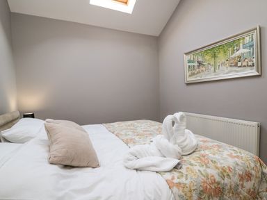 A bedroom with a bed featuring a beige pillow and floral bedspread two towel swans on the bed a painting on the wall and a skylight at Mynydd ar Mor in Barmouth