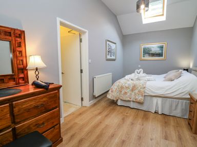A bedroom with a bed and wooden dresser with a lamp and hairdryer at Mynydd ar Mor in Barmouth