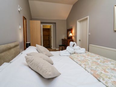 A bedroom with a bed with pillows and towels shaped like swans a dresser with a lamp and mirror at Mynydd ar Mor in Barmouth