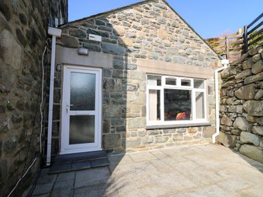An outdoor stone patio area with a white door and window set in a stone wall at Mynydd ar Mor in Barmouth