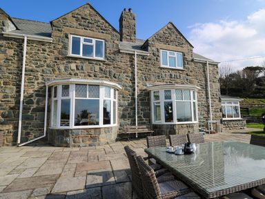 Stone house with large windows and an outdoor dining table with chairs and coffee set on patio at Mynydd ar Mor in Barmouth