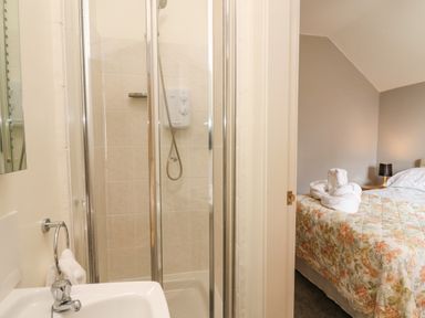 A bathroom with a shower stall and sink next to a bedroom with a bed covered in a floral patterned quilt at Mynydd ar Mor in Barmouth