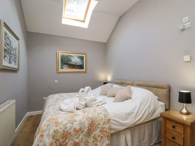 A bedroom with a bed with floral bedding and pillows a wooden nightstand with a lamp and framed pictures on the walls at Mynydd ar Mor in Barmouth