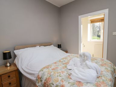 A bedroom with a bed covered in white sheets and floral bedding with towel swans on top at Mynydd ar Mor in Barmouth